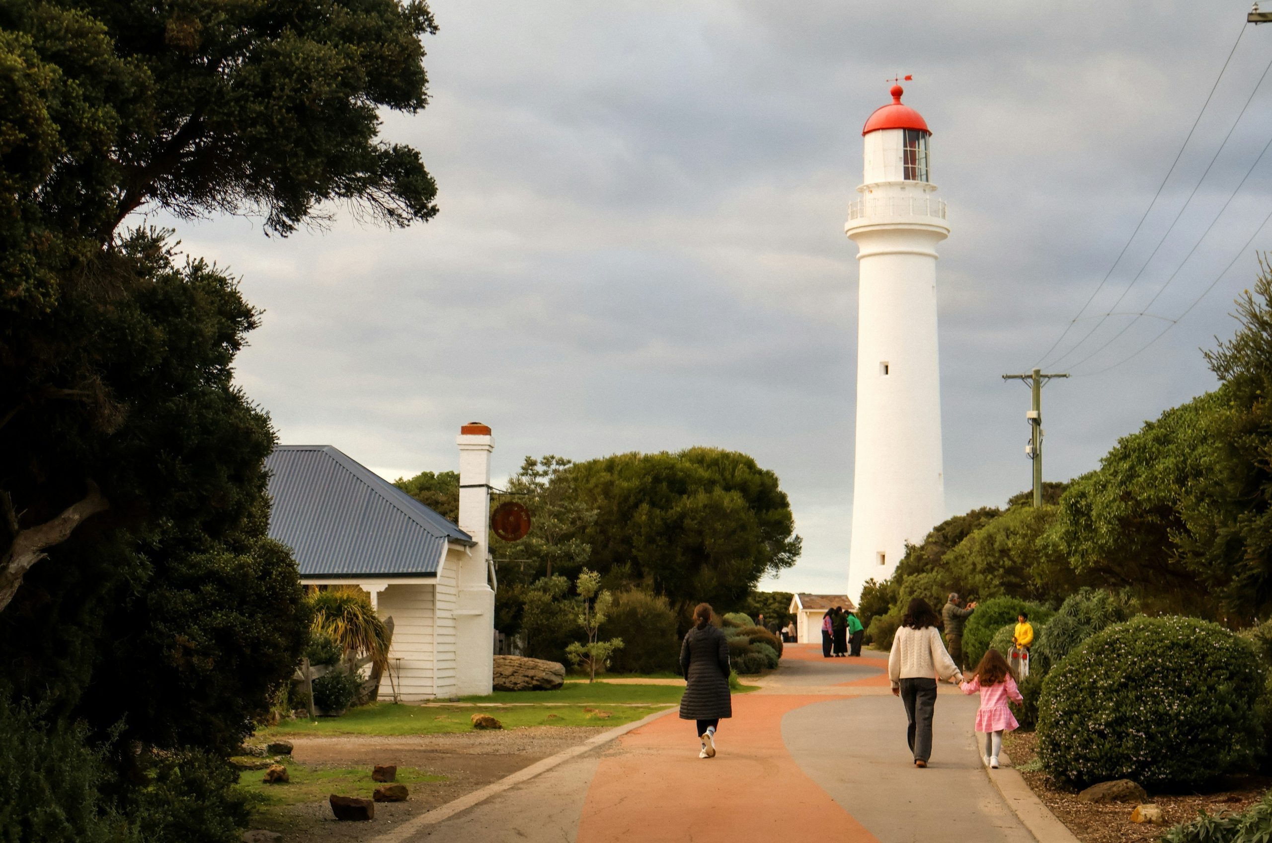 Visitors walk on a path towards a tall white lighthouse.