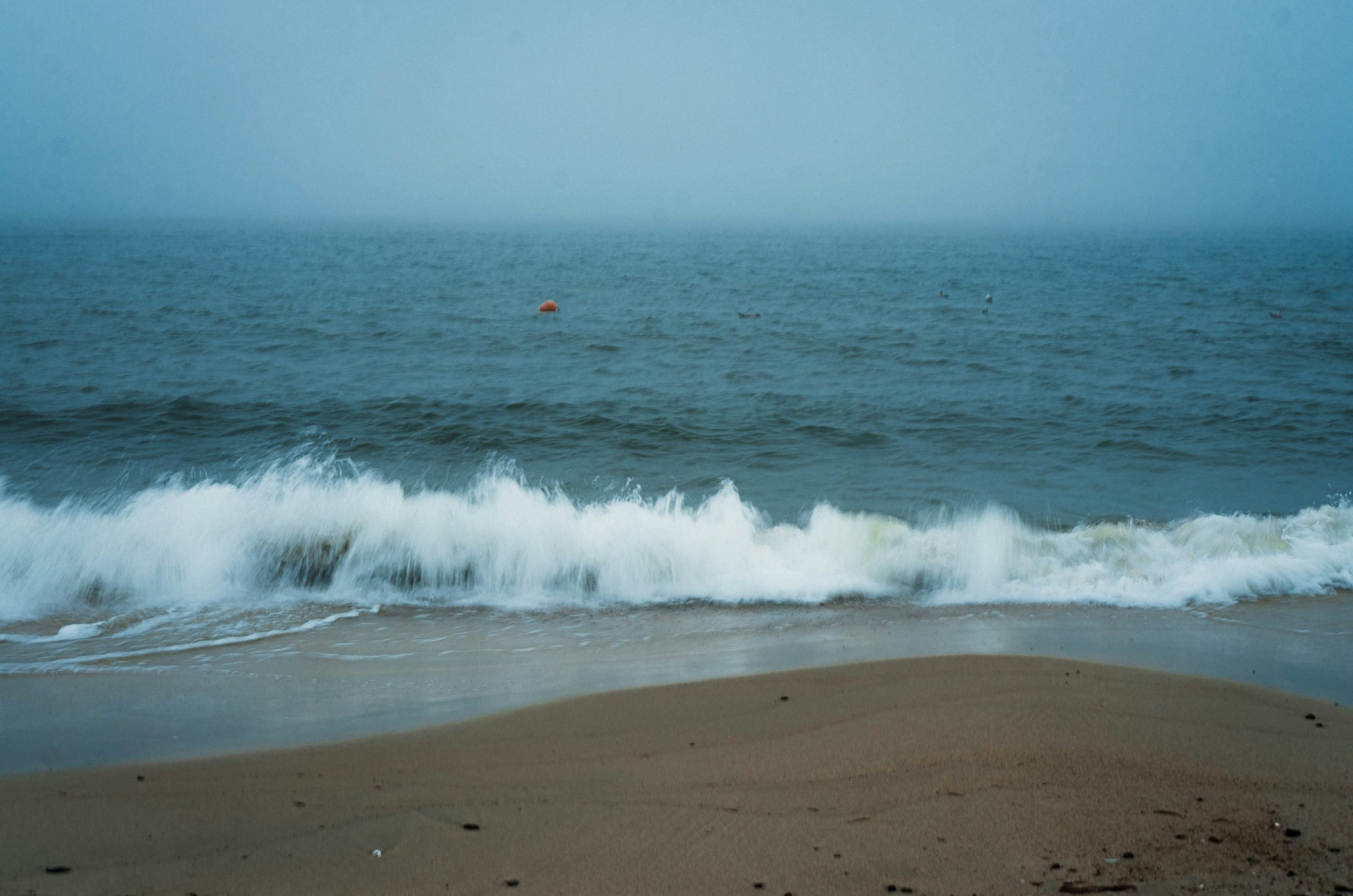 Waves crash on a sandy beach under a foggy sky.