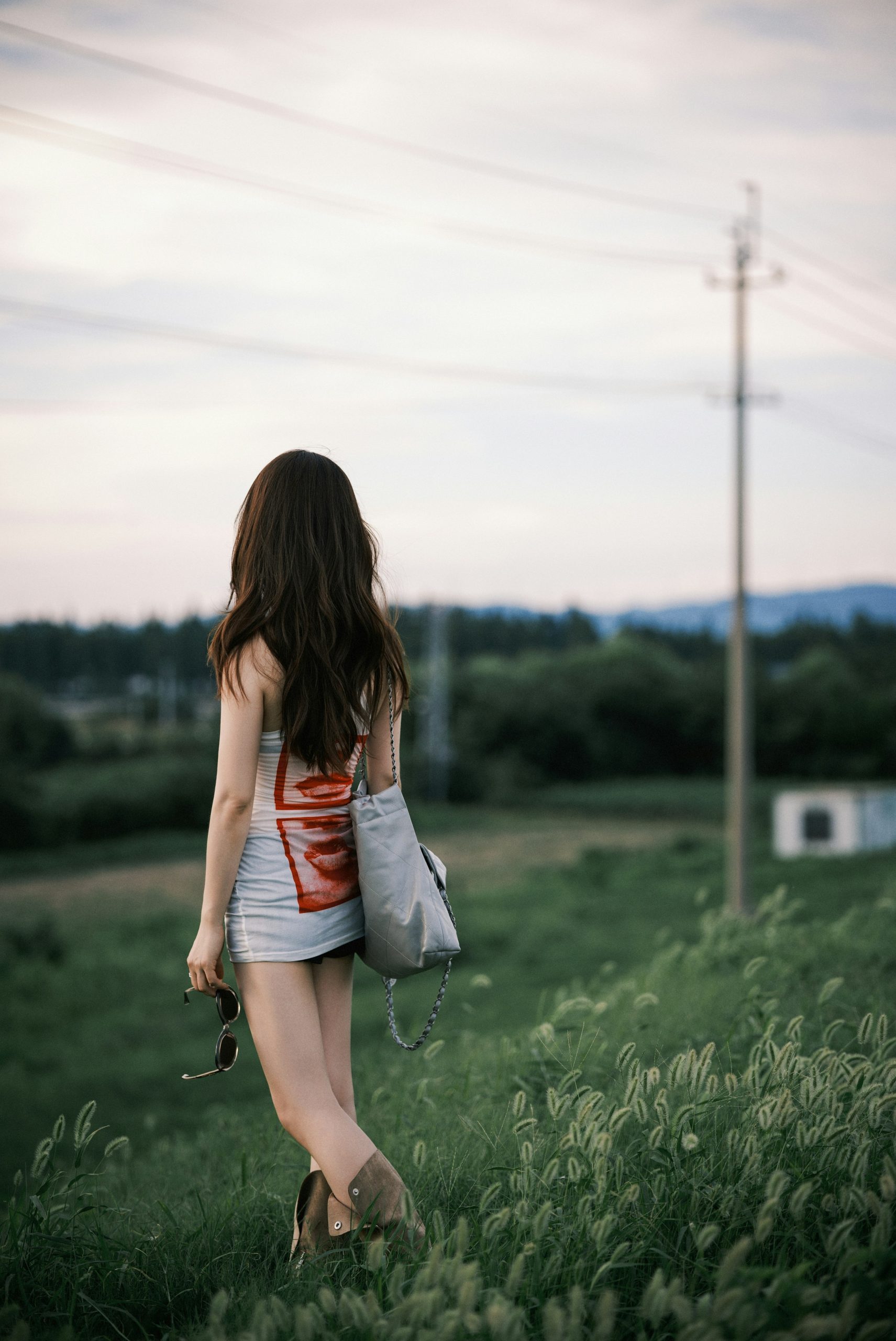 Woman walking away in a grassy field at dusk.