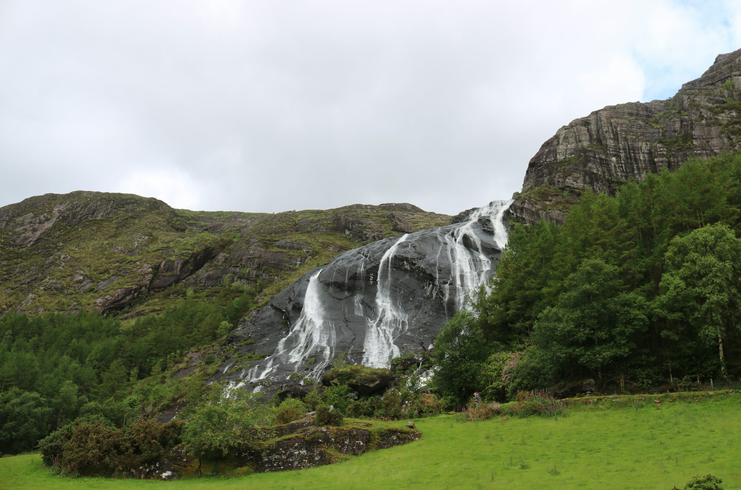 Waterfall cascades down rocky mountain with green landscape.