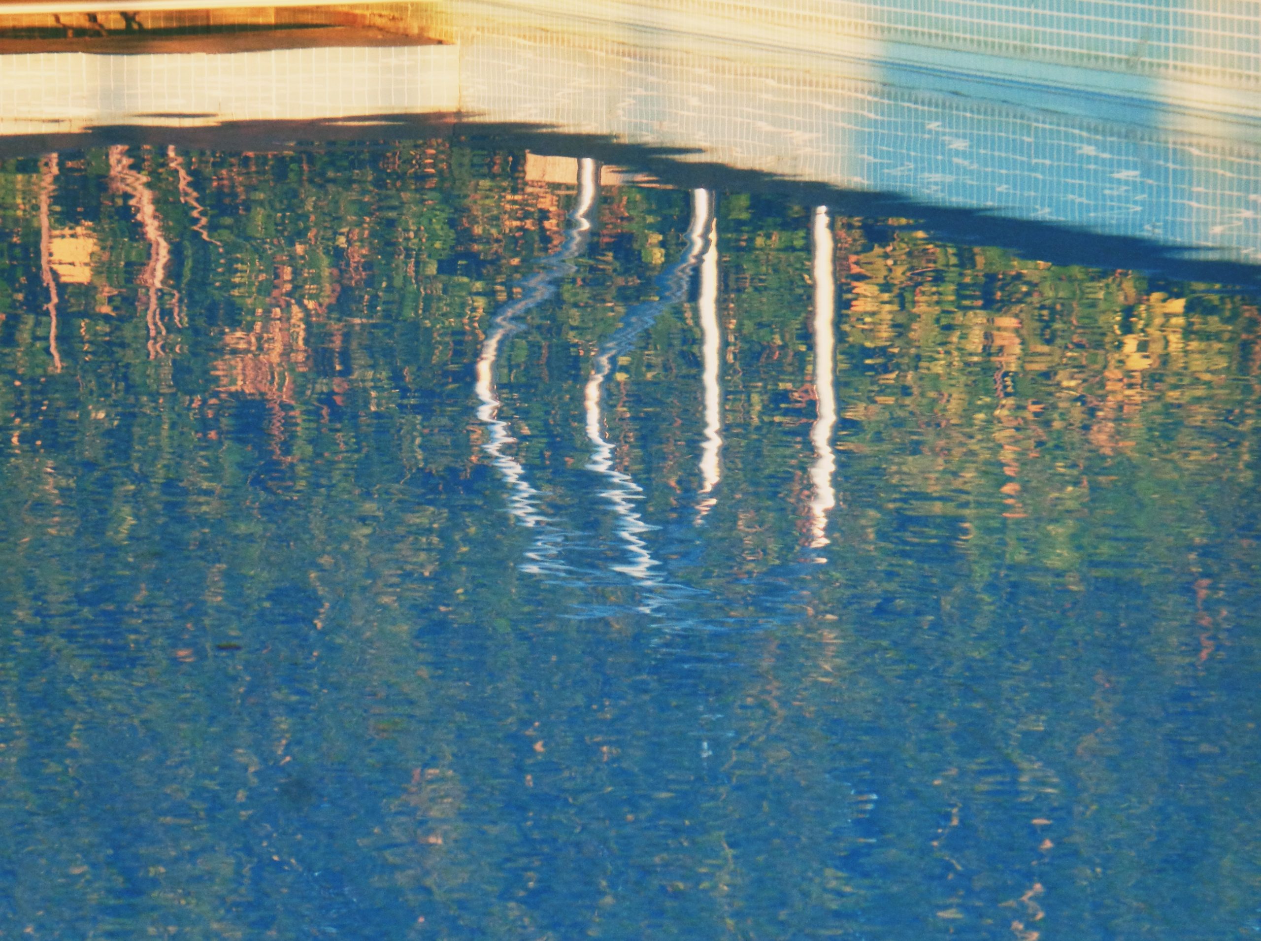 Wavy reflections of a structure and trees on blue water.