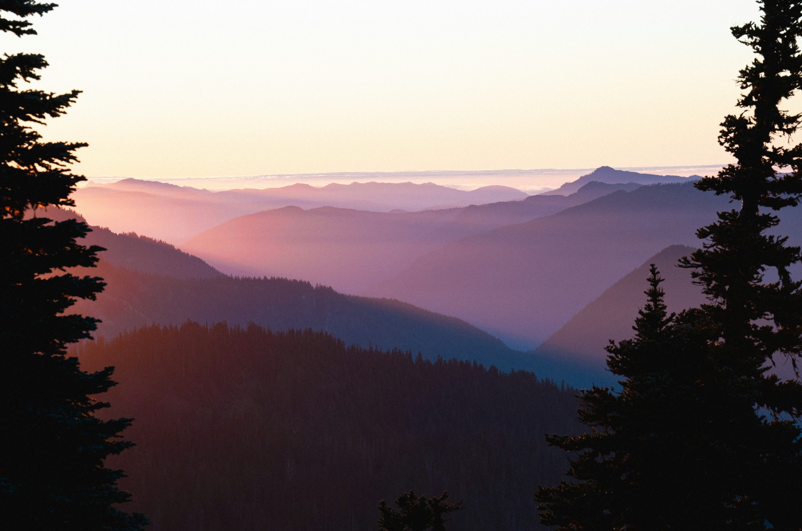 Vibrant sunset over layered mountains with tree silhouettes.