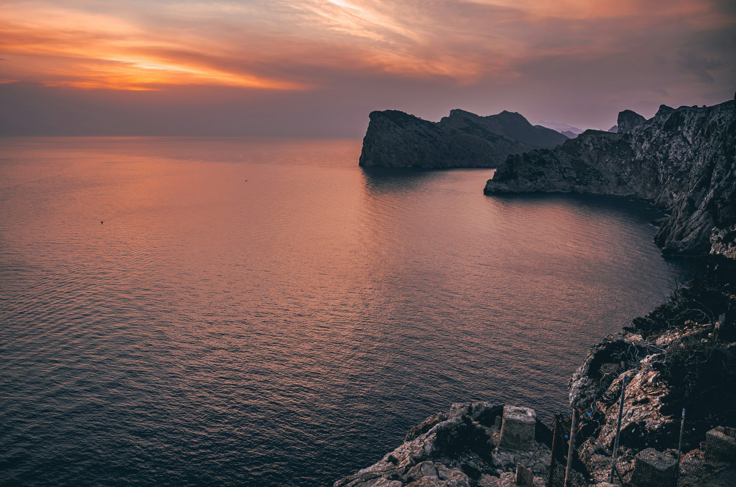 Vibrant sunset sky illuminates rugged cliffs and serene ocean.