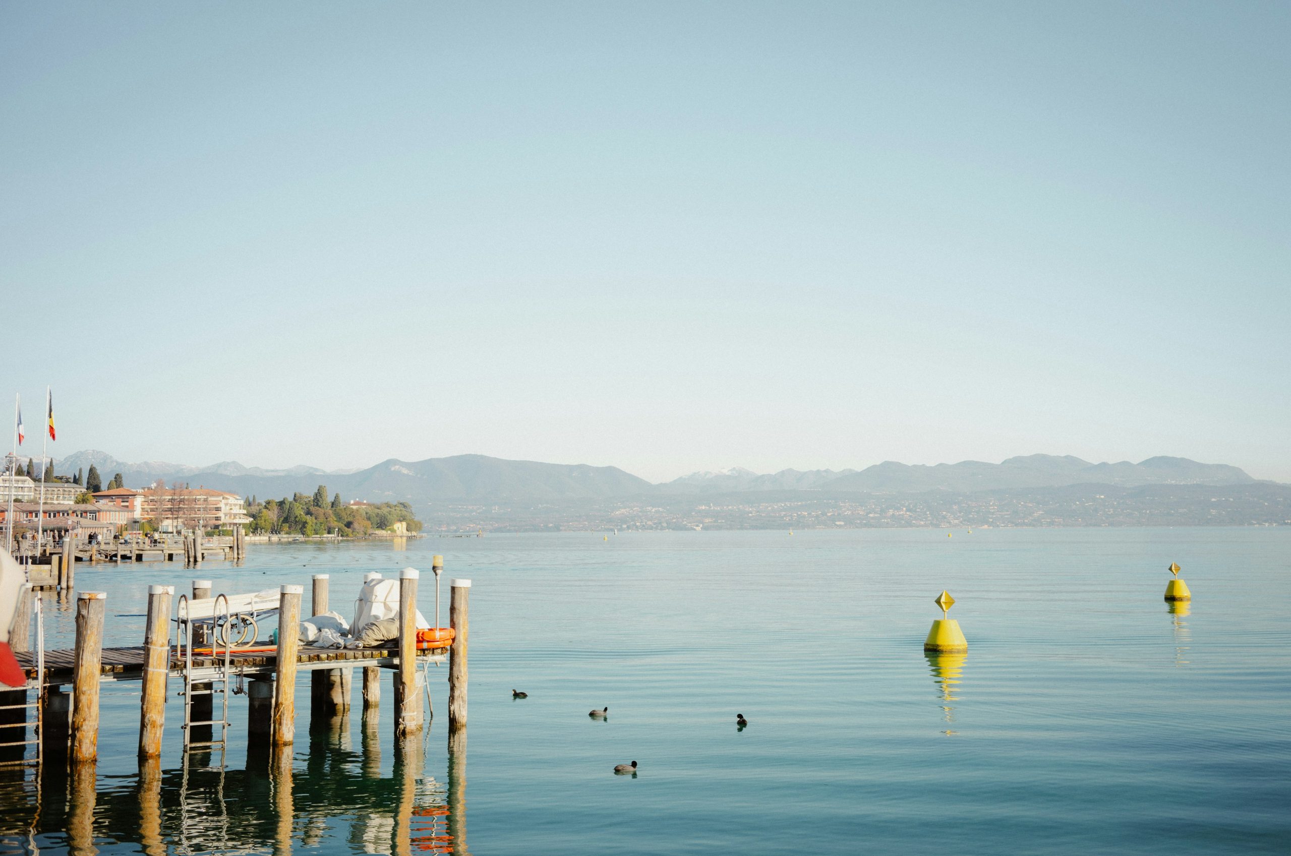A wooden pier on a calm lake with yellow buoys and distant mountains.