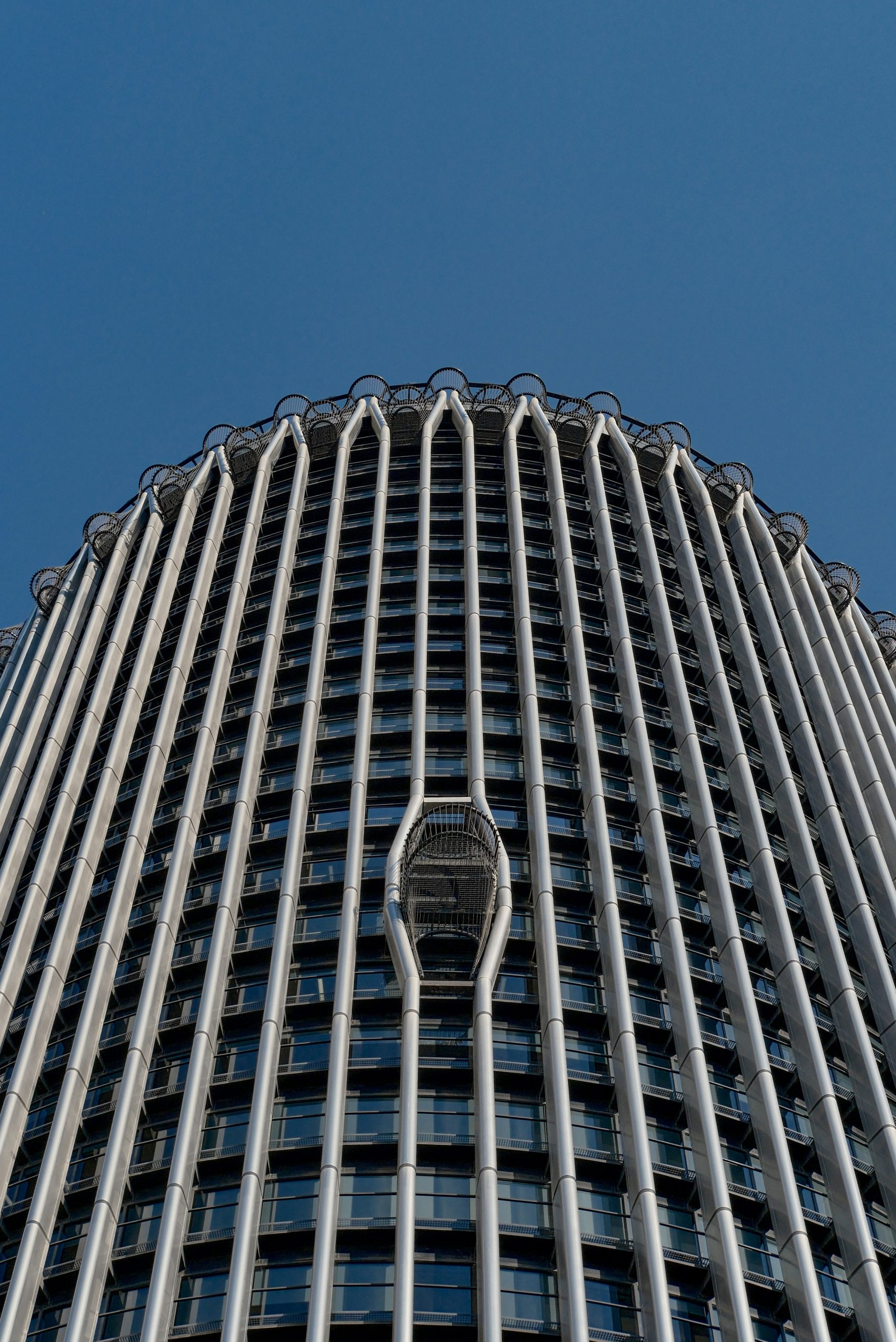 A cylindrical skyscraper with vertical metal fins against a clear blue sky.
