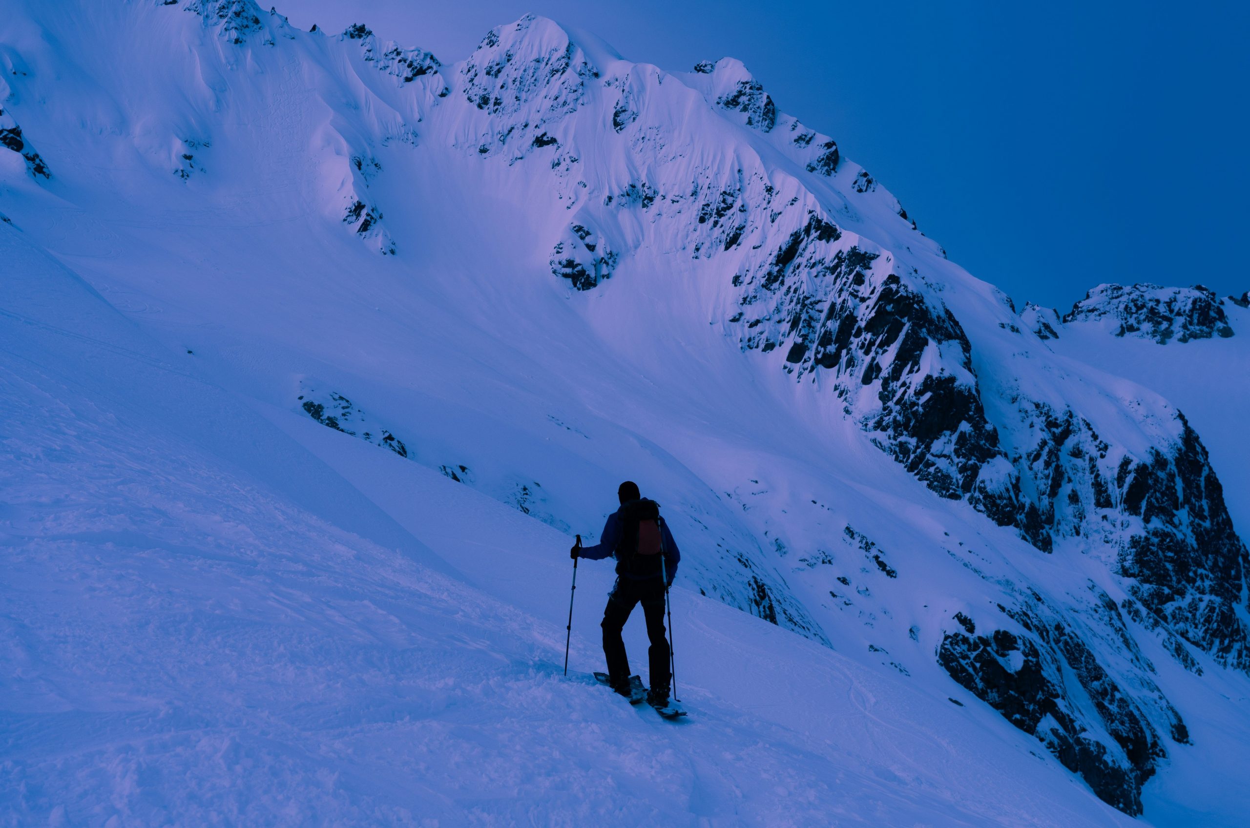 Backcountry skier ascends a snowy mountain peak.