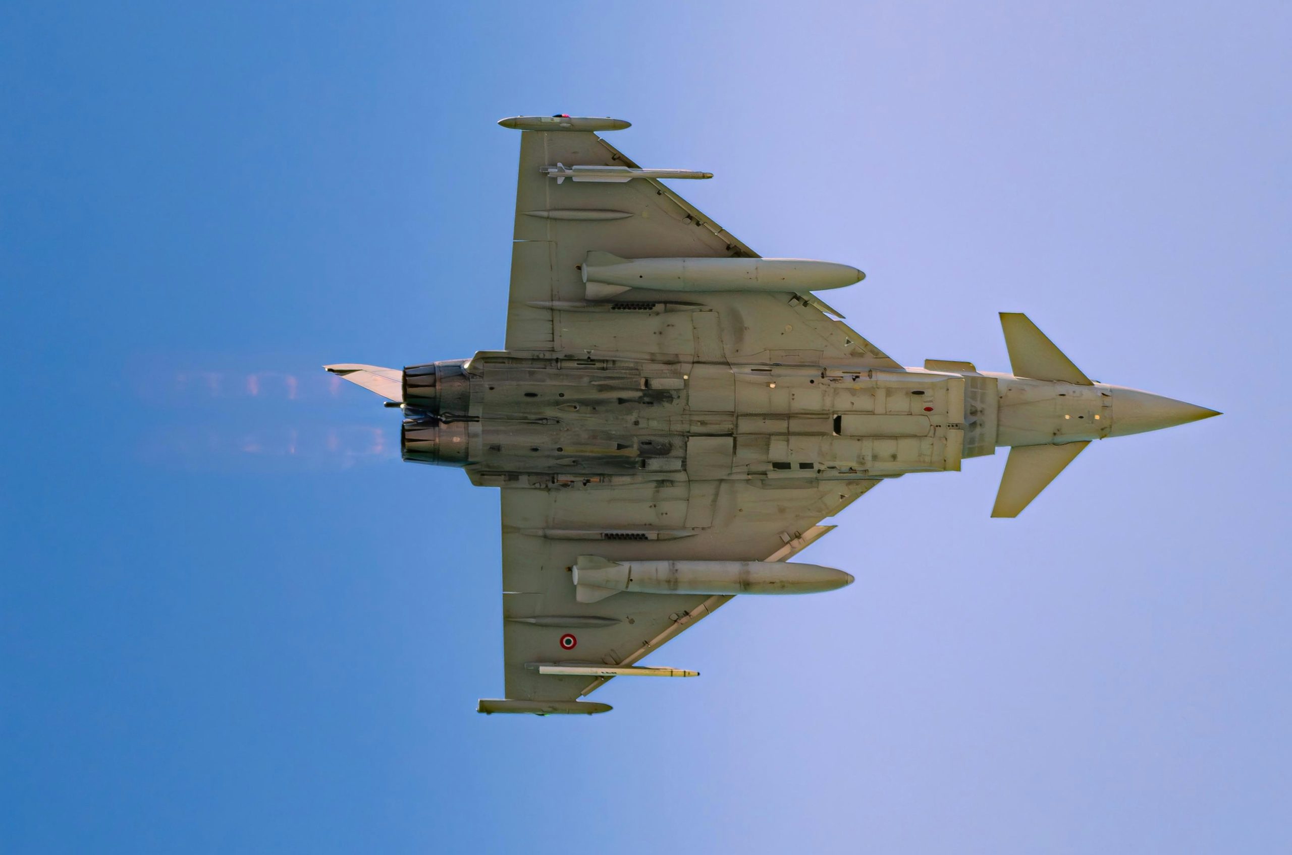A fighter jet flies through a clear blue sky.
