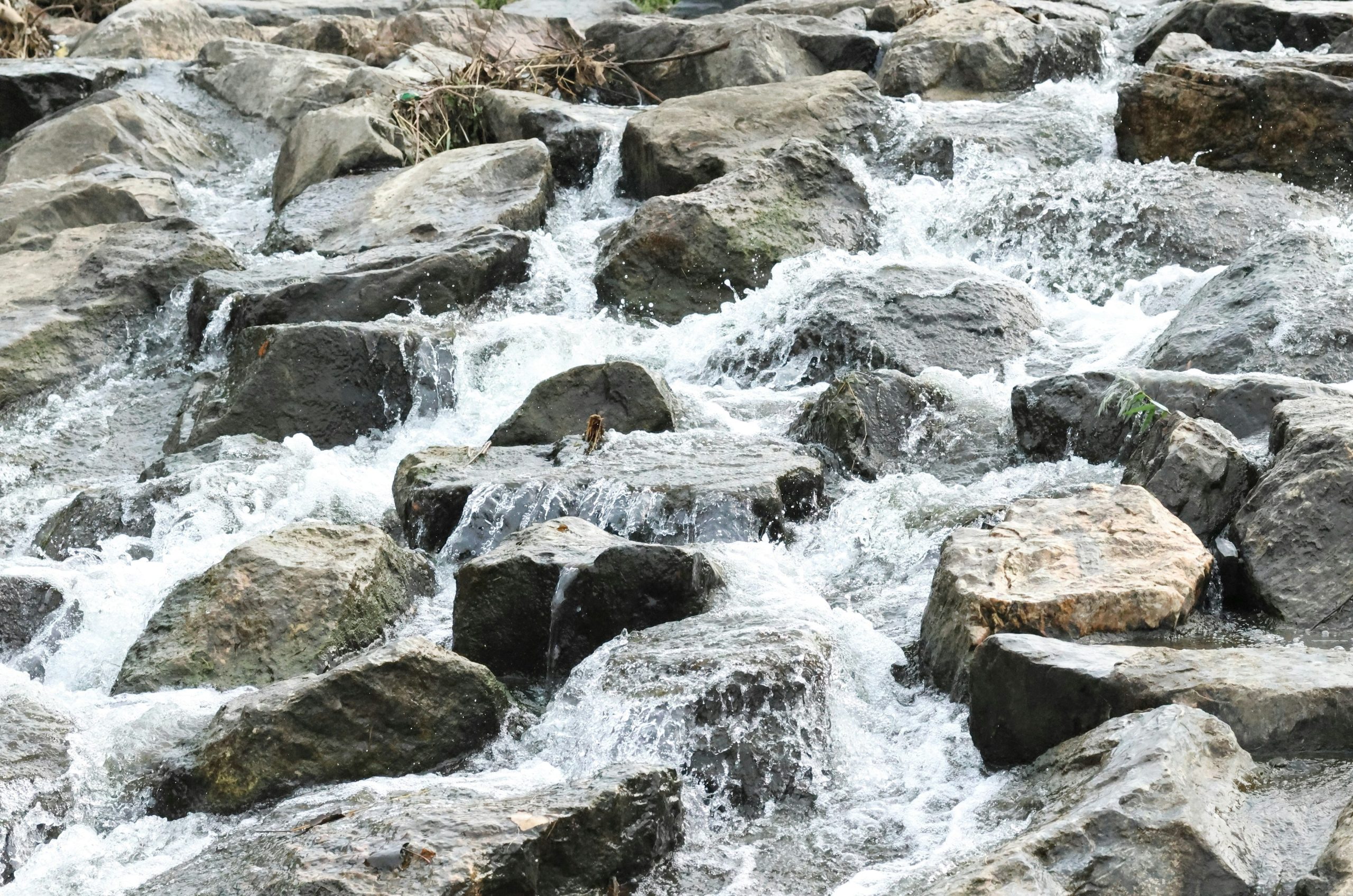 A small waterfall cascades over numerous grey rocks.