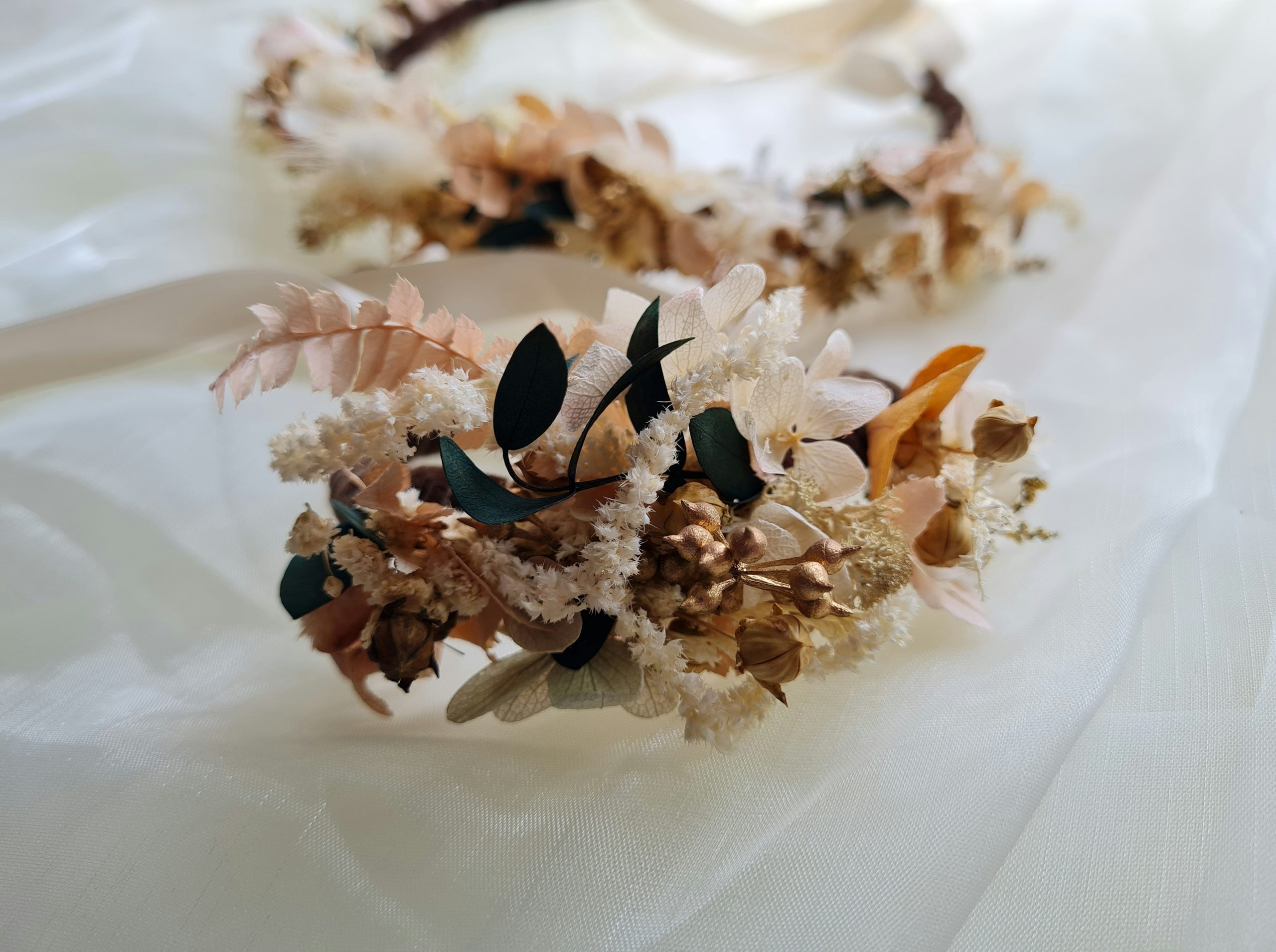 Two floral crowns made of dried flowers and leaves on a white fabric.