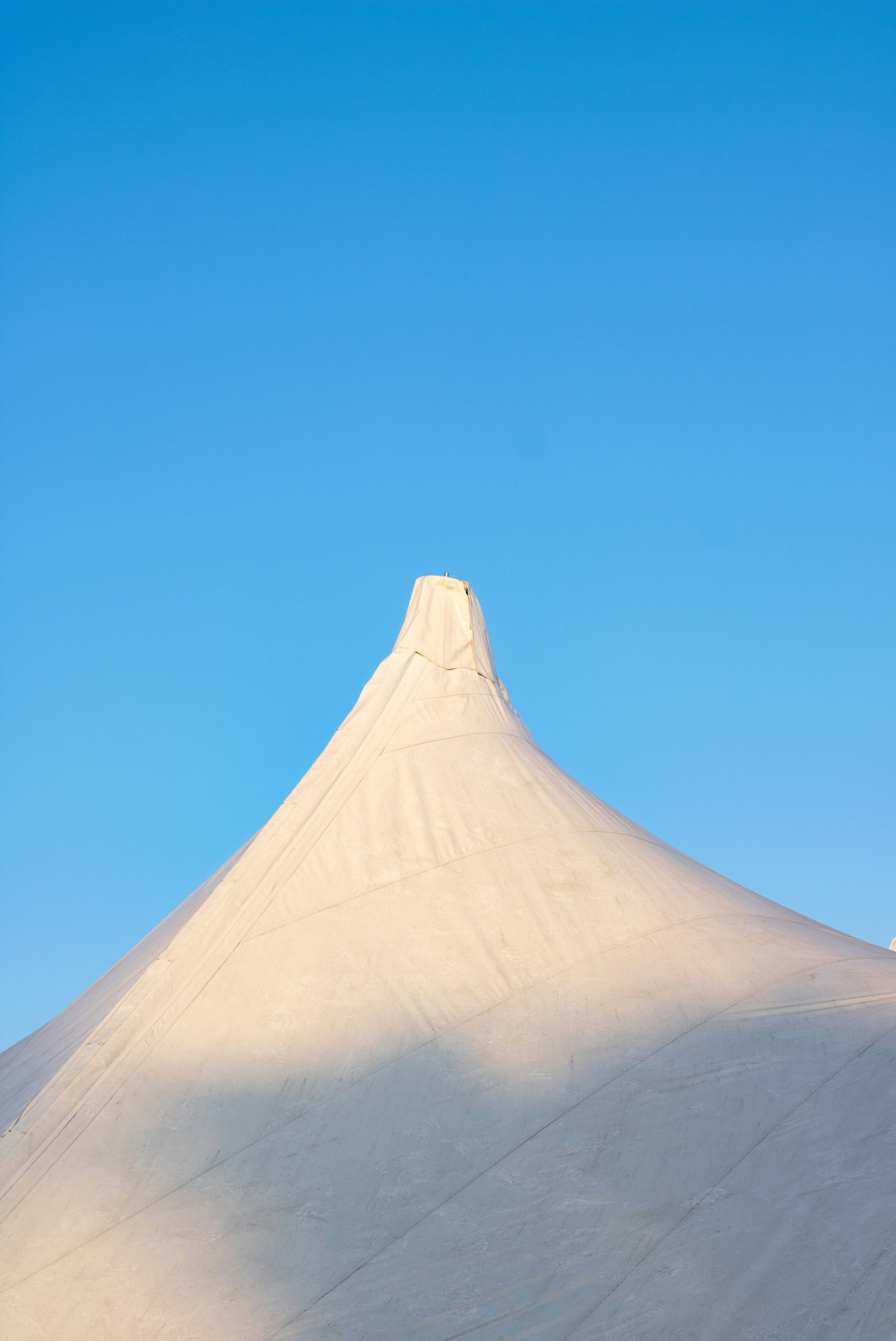 A white fabric tent peak against a clear blue sky.