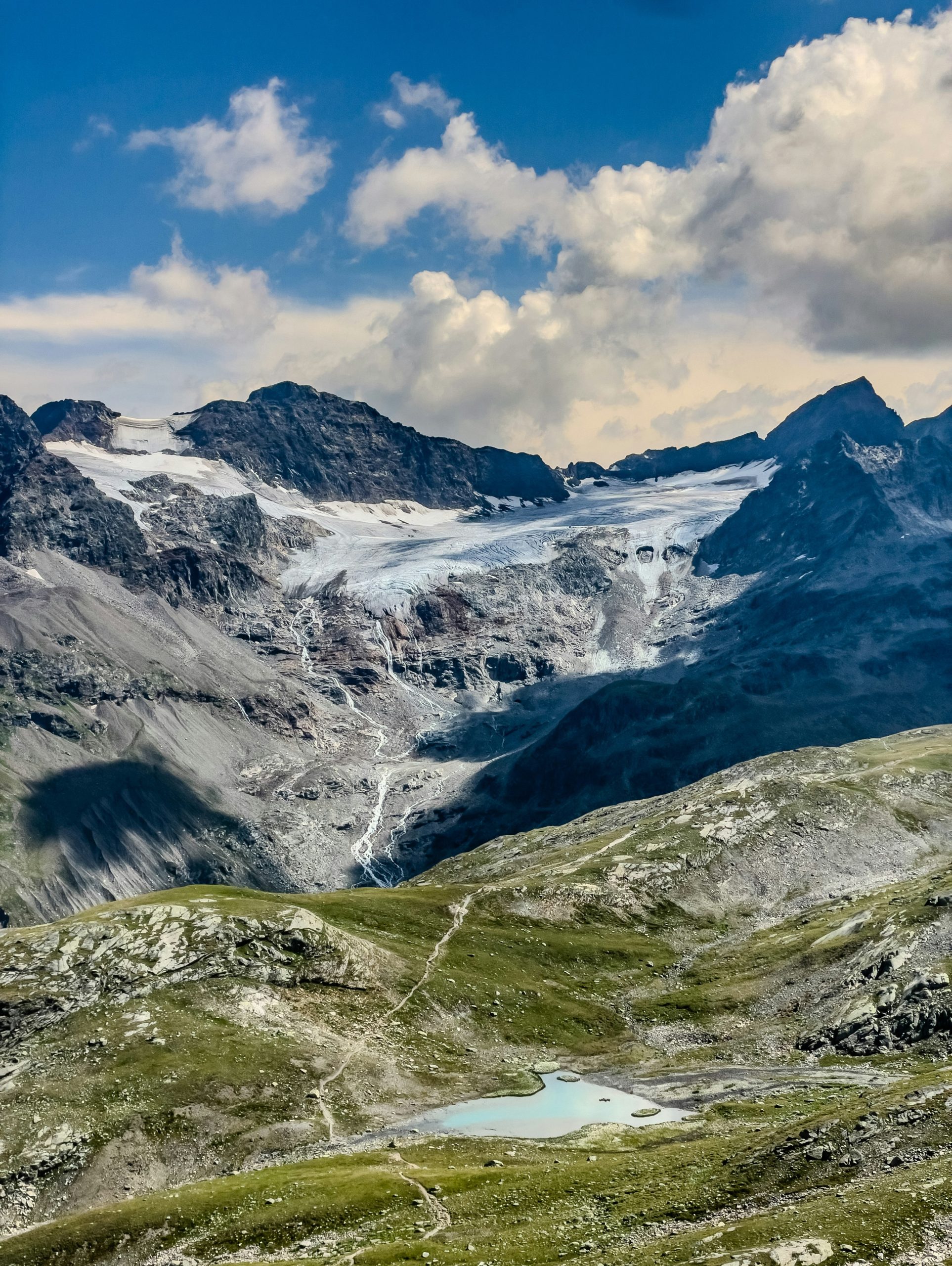 A glacier flowing down a rocky mountain slope toward a small turquoise lake.