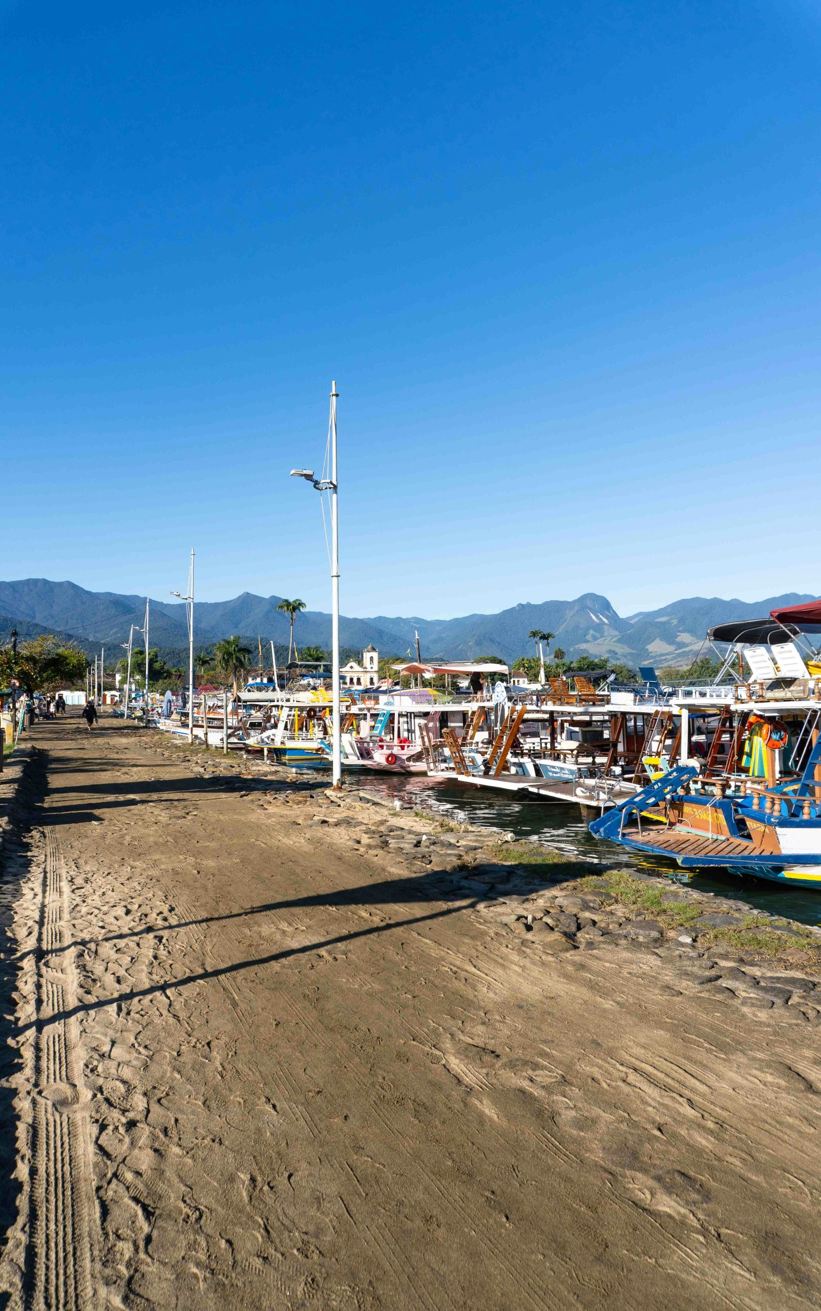 Boats moored along a sandy waterfront with mountains in the distance.