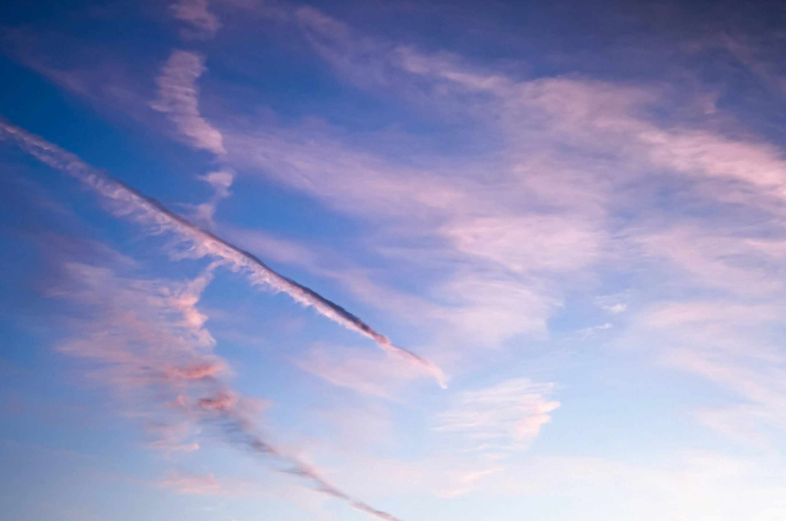 Pink and blue clouds with a long vapor trail across the sky.