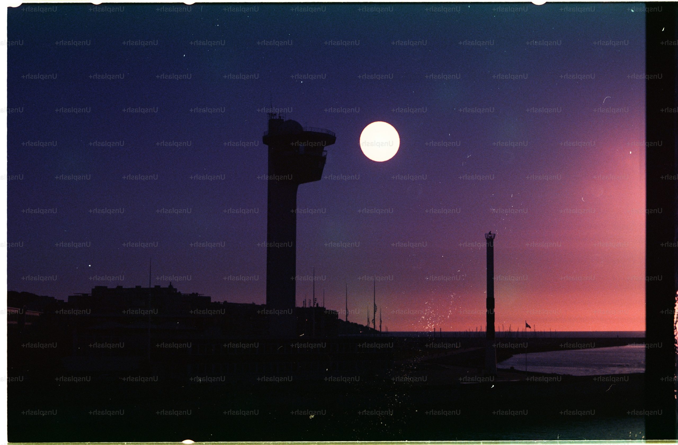 A tall control tower silhouetted against a bright moon and a dark purple sky.