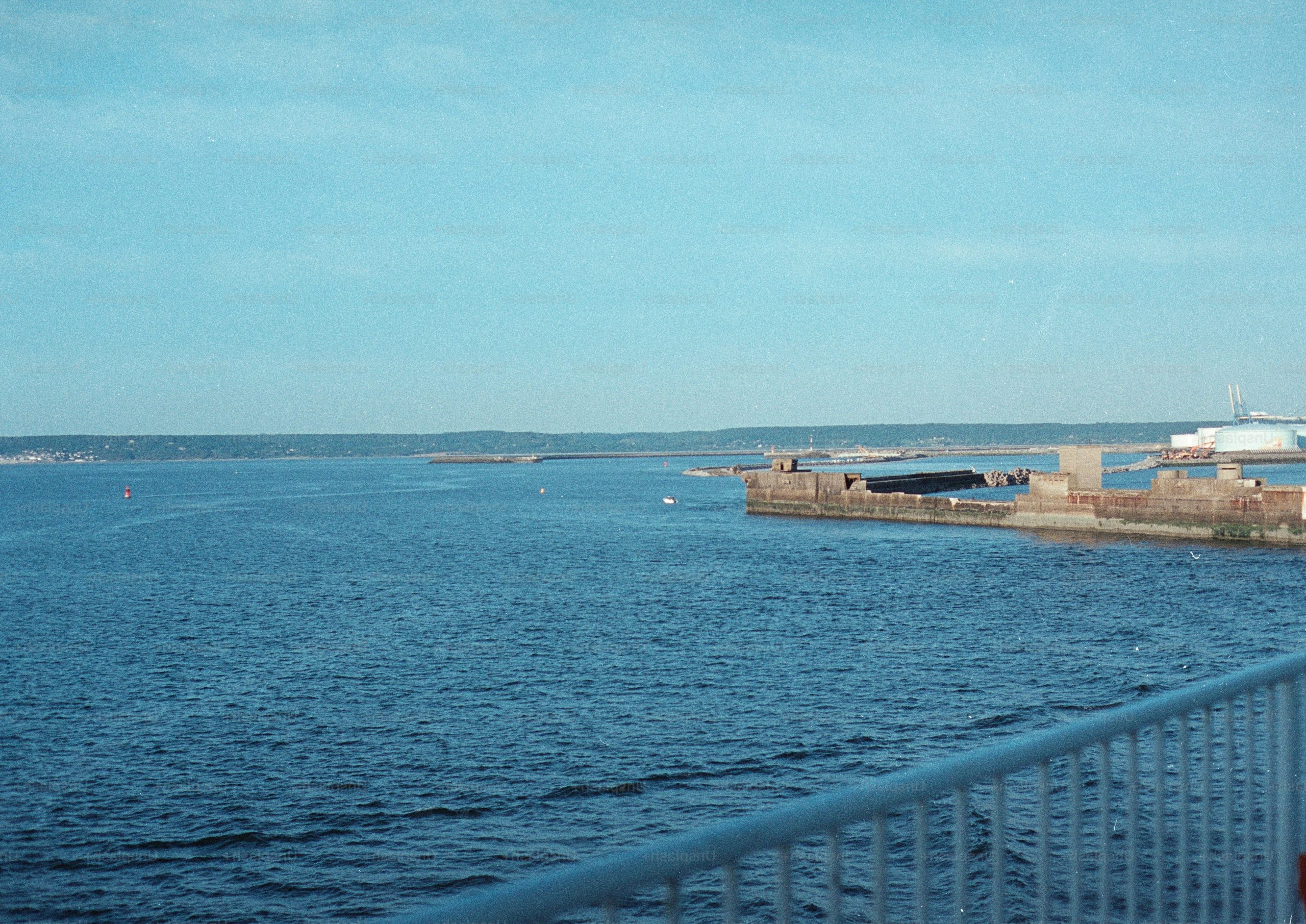 A stone breakwater extending into a calm blue bay under a clear sky.