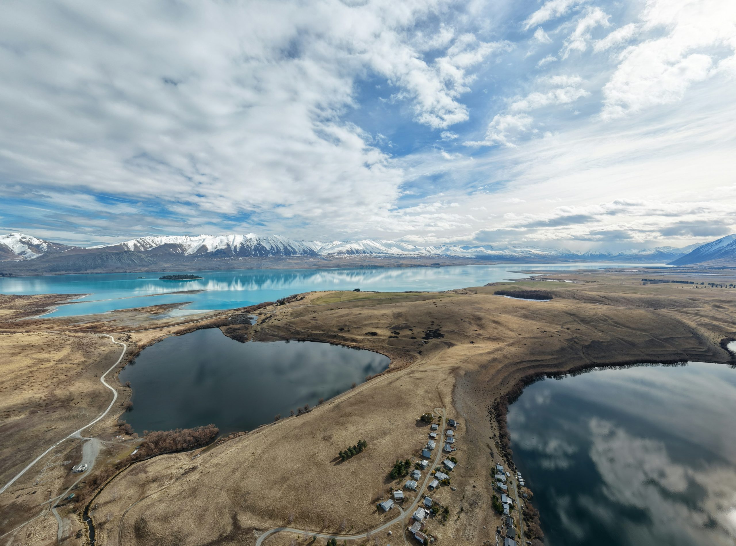 An aerial view of Lake Tekapo with snow-capped mountains under a cloudy sky.