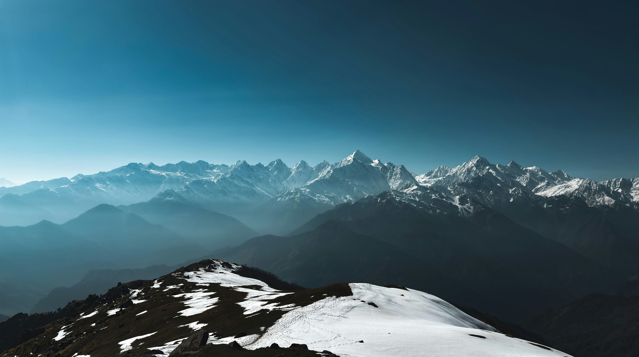 Snow-capped mountain peaks rising above a dark, misty valley under a clear blue sky.