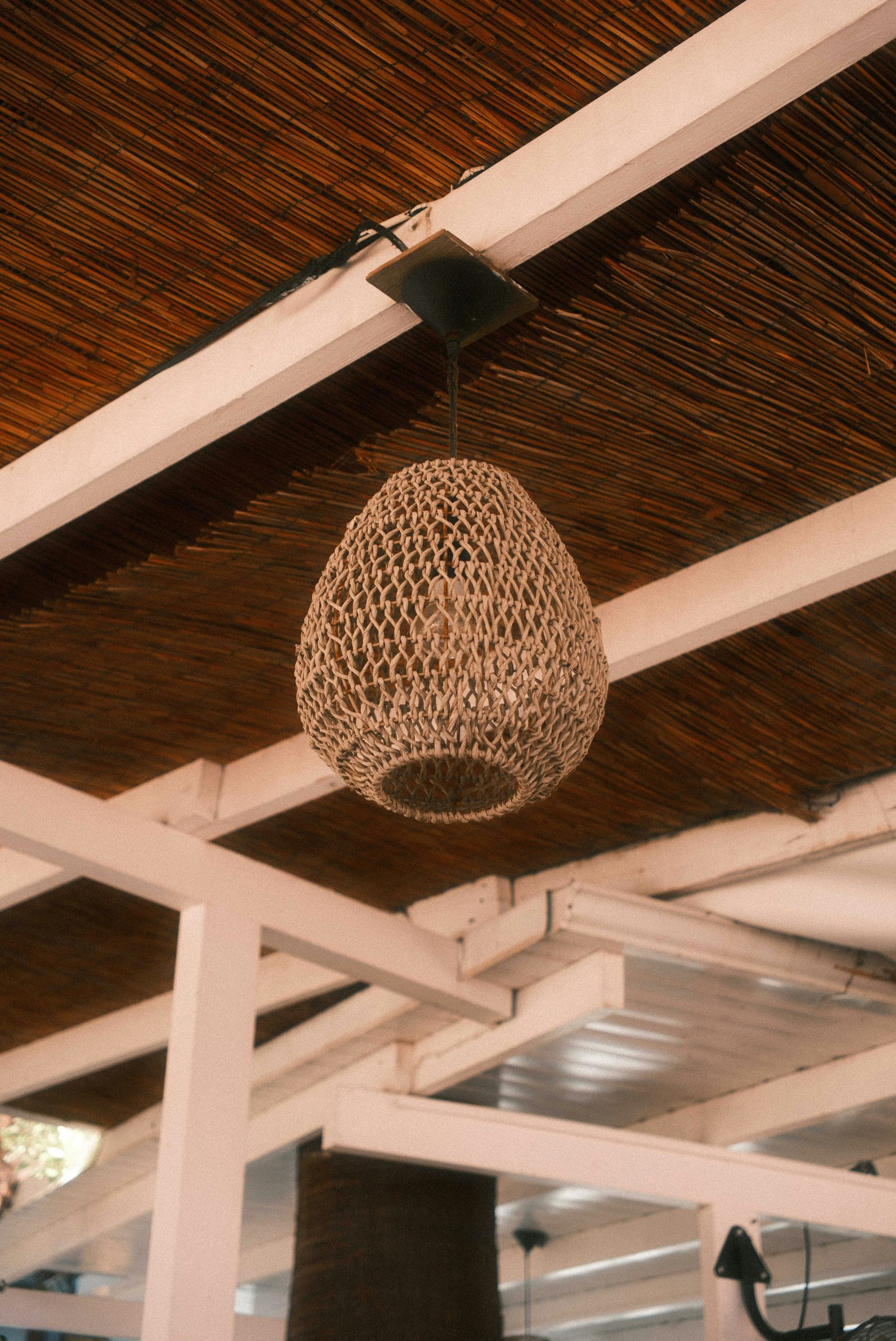 A woven rattan pendant light hanging from a slatted wooden ceiling.