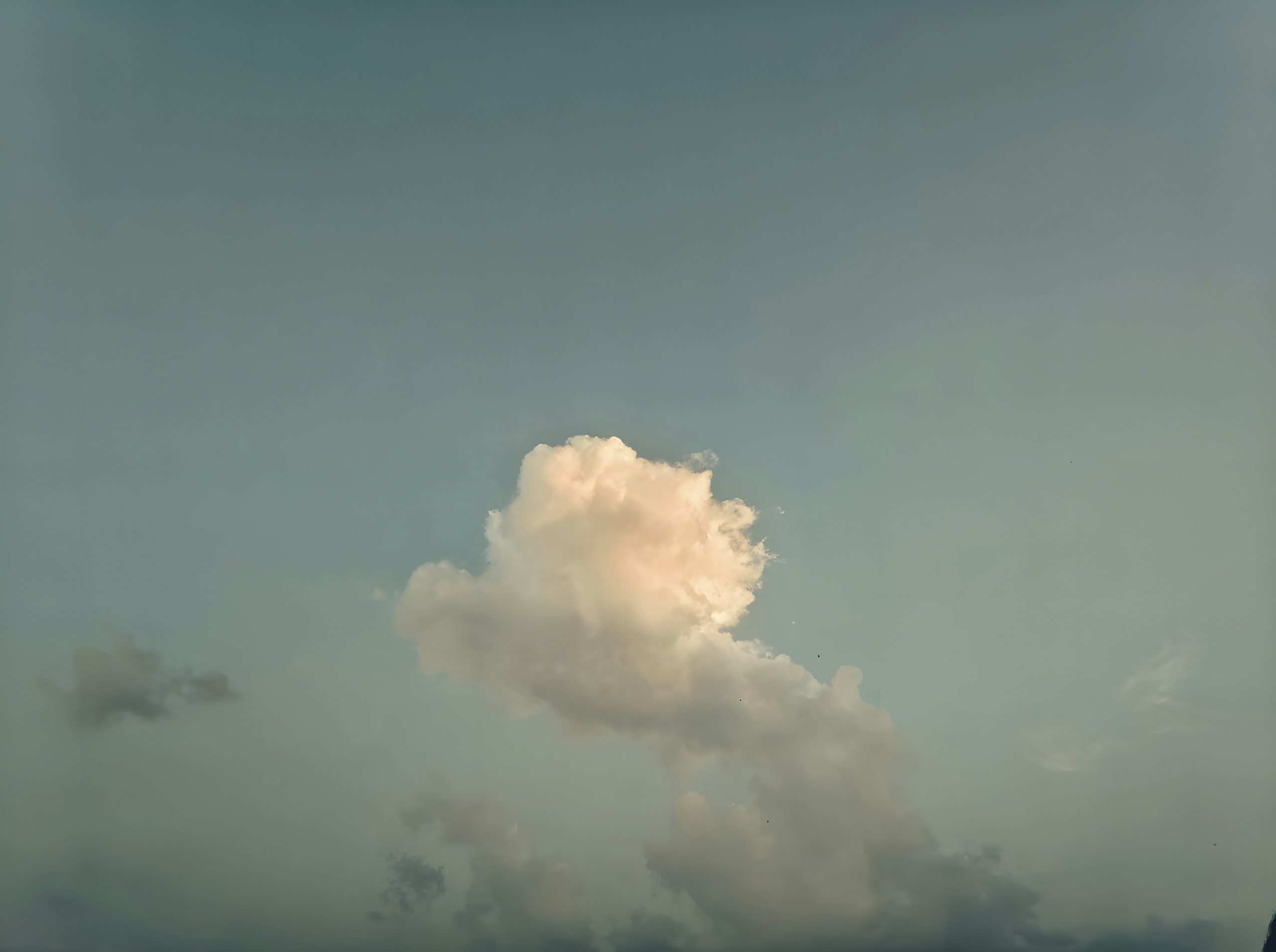 A single sunlit white cloud against a pale blue sky.