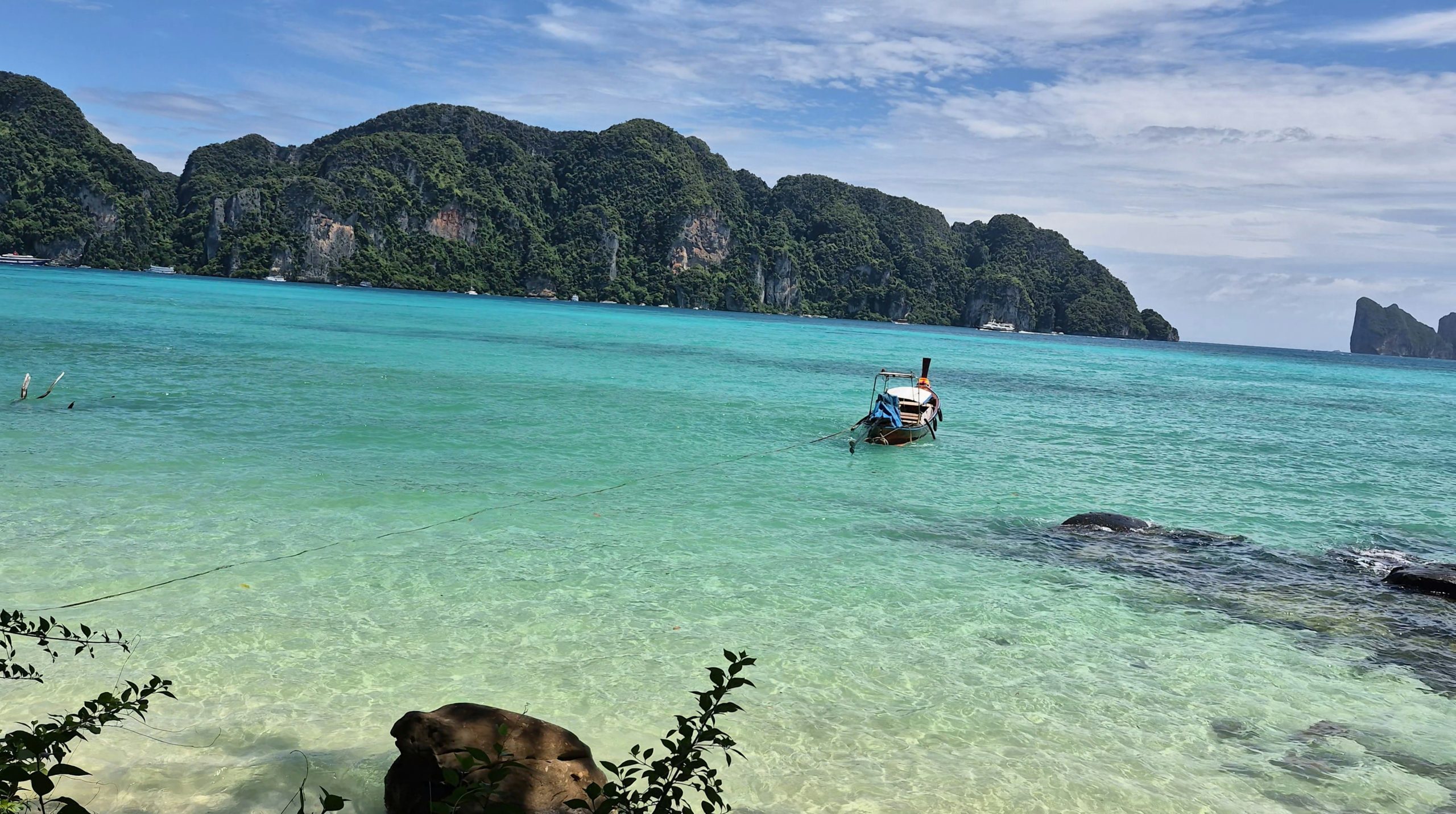 A long-tail boat floating in clear turquoise water near limestone cliffs in Thailand.