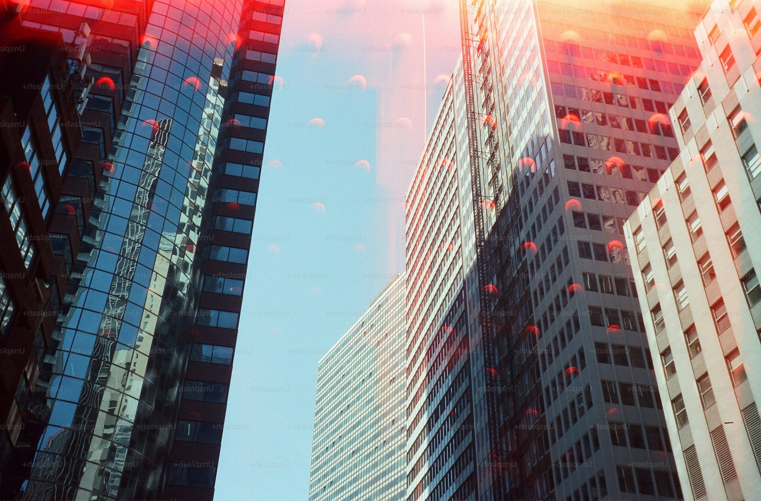 Double exposure of skyscrapers in New York with red light leaks and blue sky.