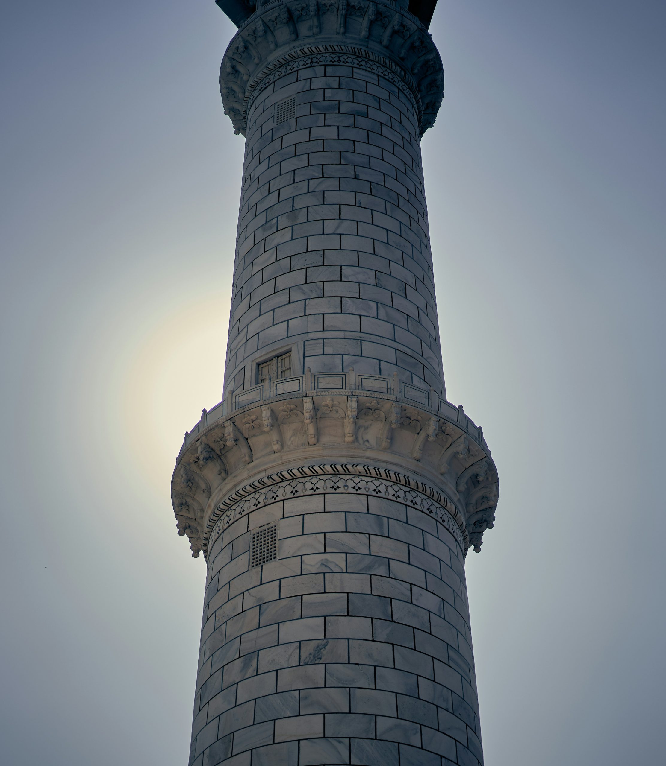 A marble minaret of the Taj Mahal silhouetted against a bright hazy sky.