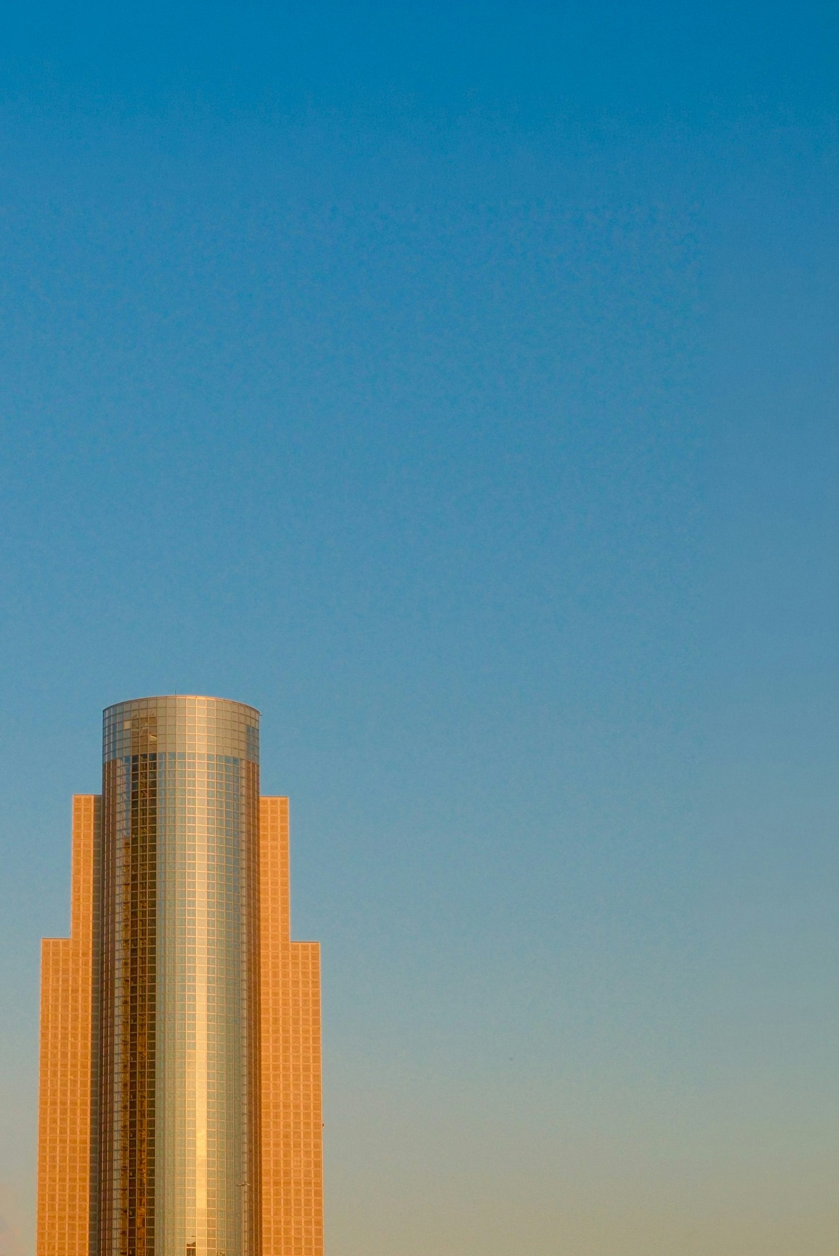 A cylindrical glass skyscraper against a clear blue sky in Sumida, Japan.