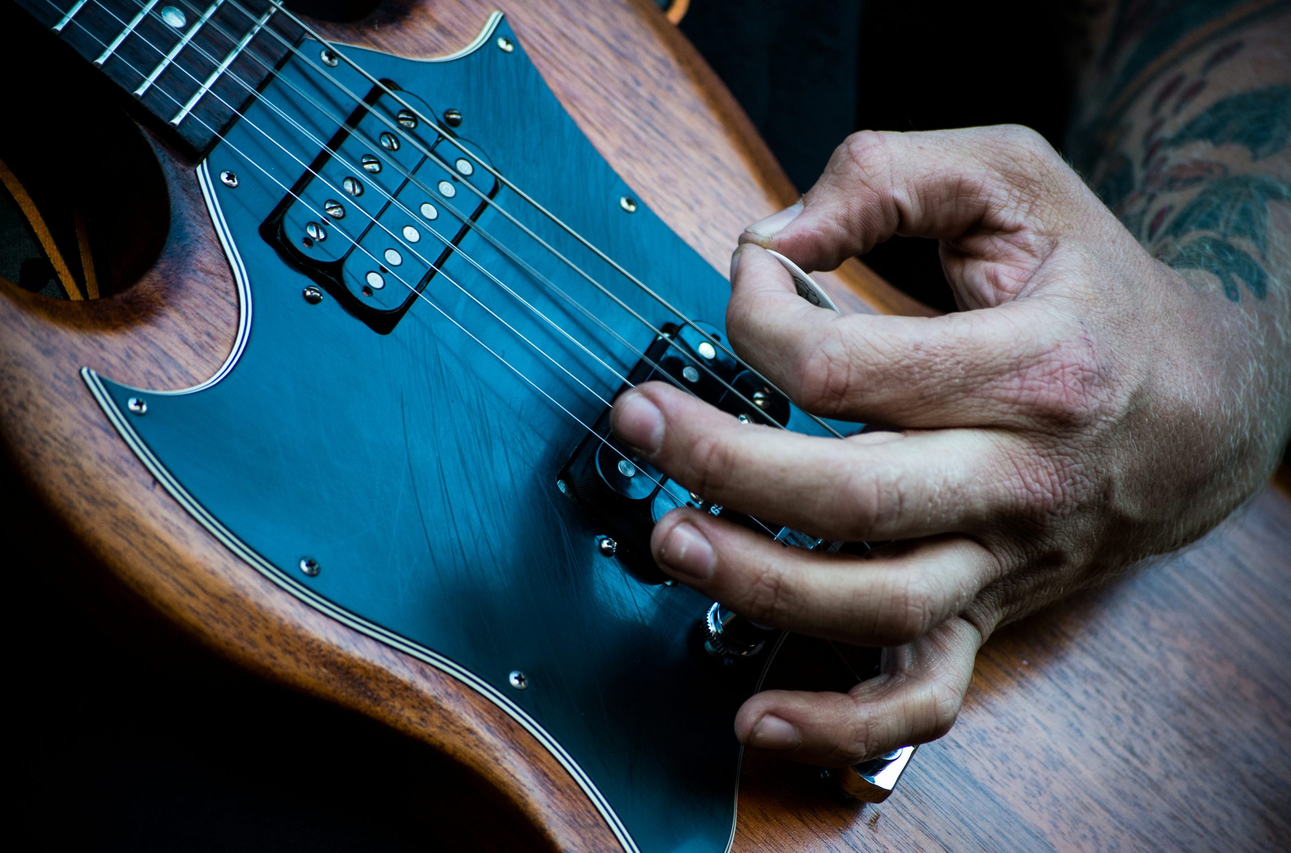 person plucking electric guitar with guitar pick