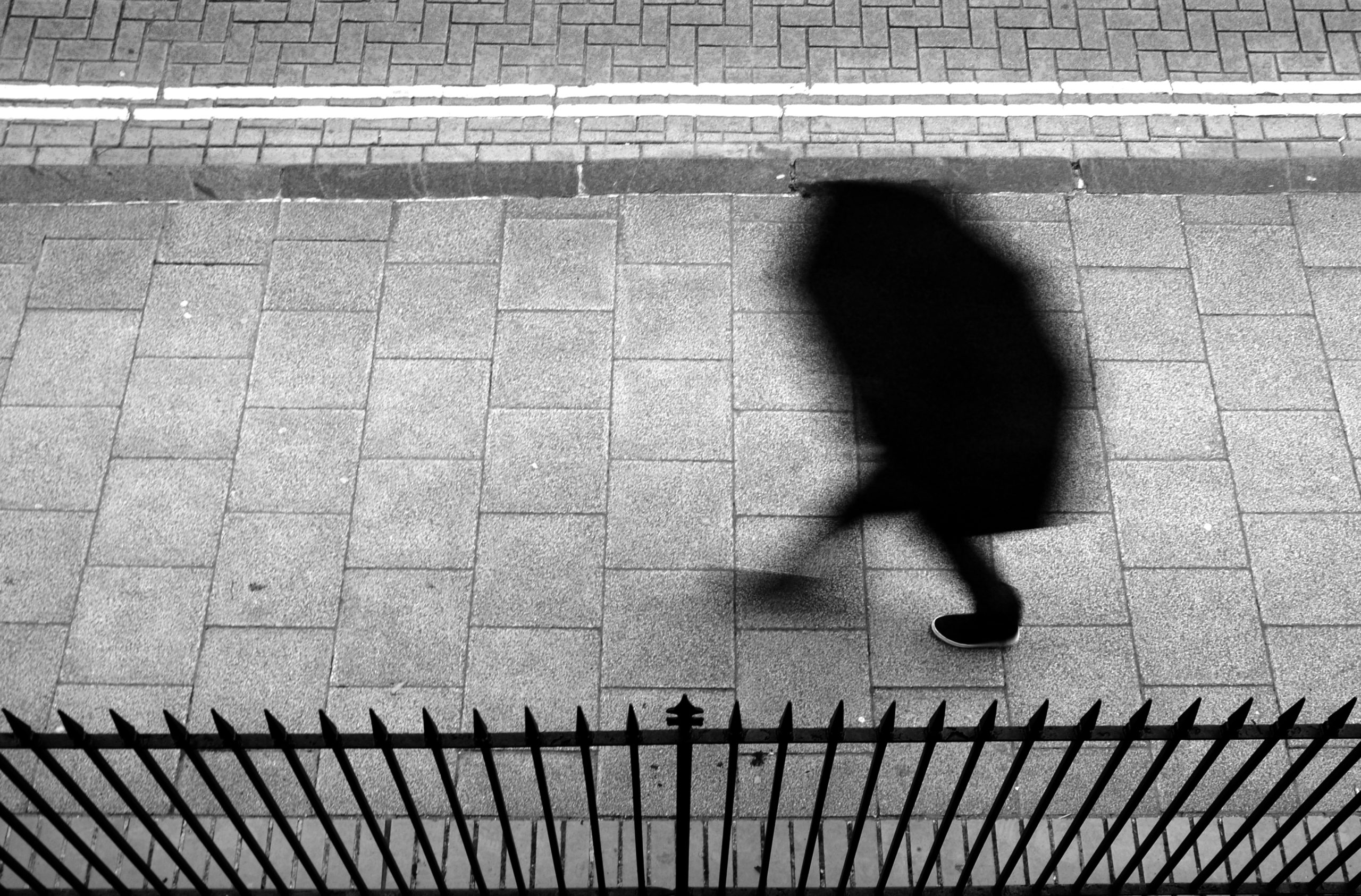 a person walking down a sidewalk next to a fence