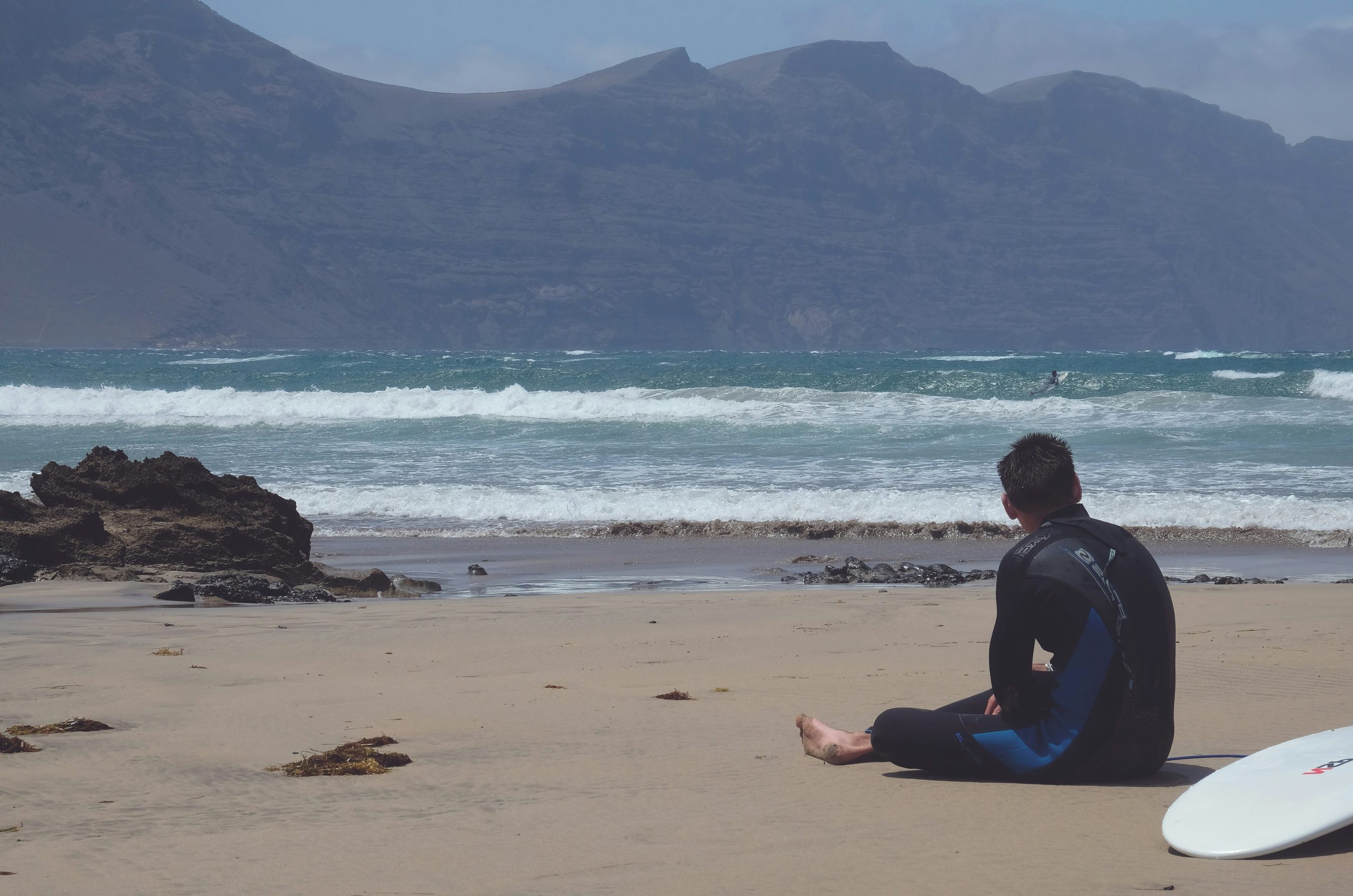 man in black shirt and blue pants sitting on beach shore during daytime